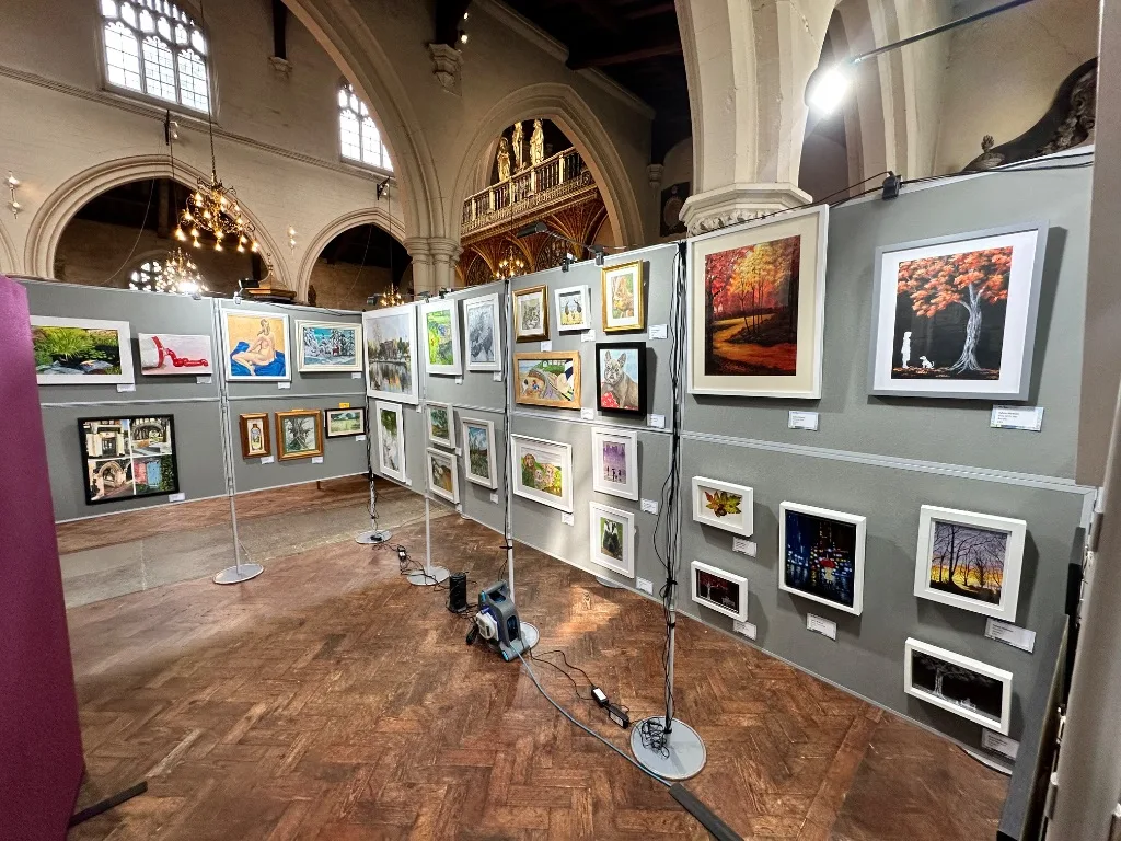 Framed paintings, including autumn trees, animals and landscapes, hung on grey display boards at a Carshalton & Wallington Art Group exhibition