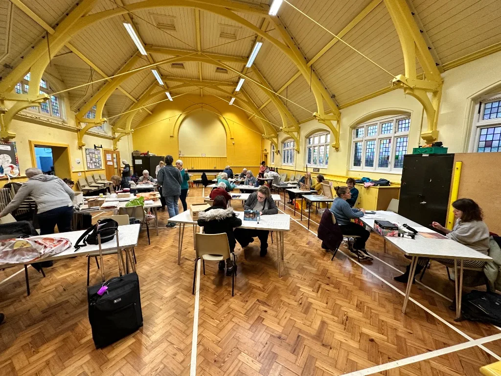 Members of the art group working at tables in a large hall with a yellow arched ceiling and tall windows
