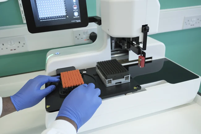 Gloved hands loading a rack of orange-capped sample tubes into laboratory equipment at The Royal Marsden